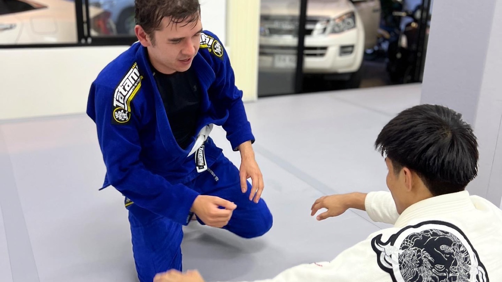 A coach guiding a beginner through a Brazilian Jiu-Jitsu escape at Gato Studio BJJ in Chiang Mai