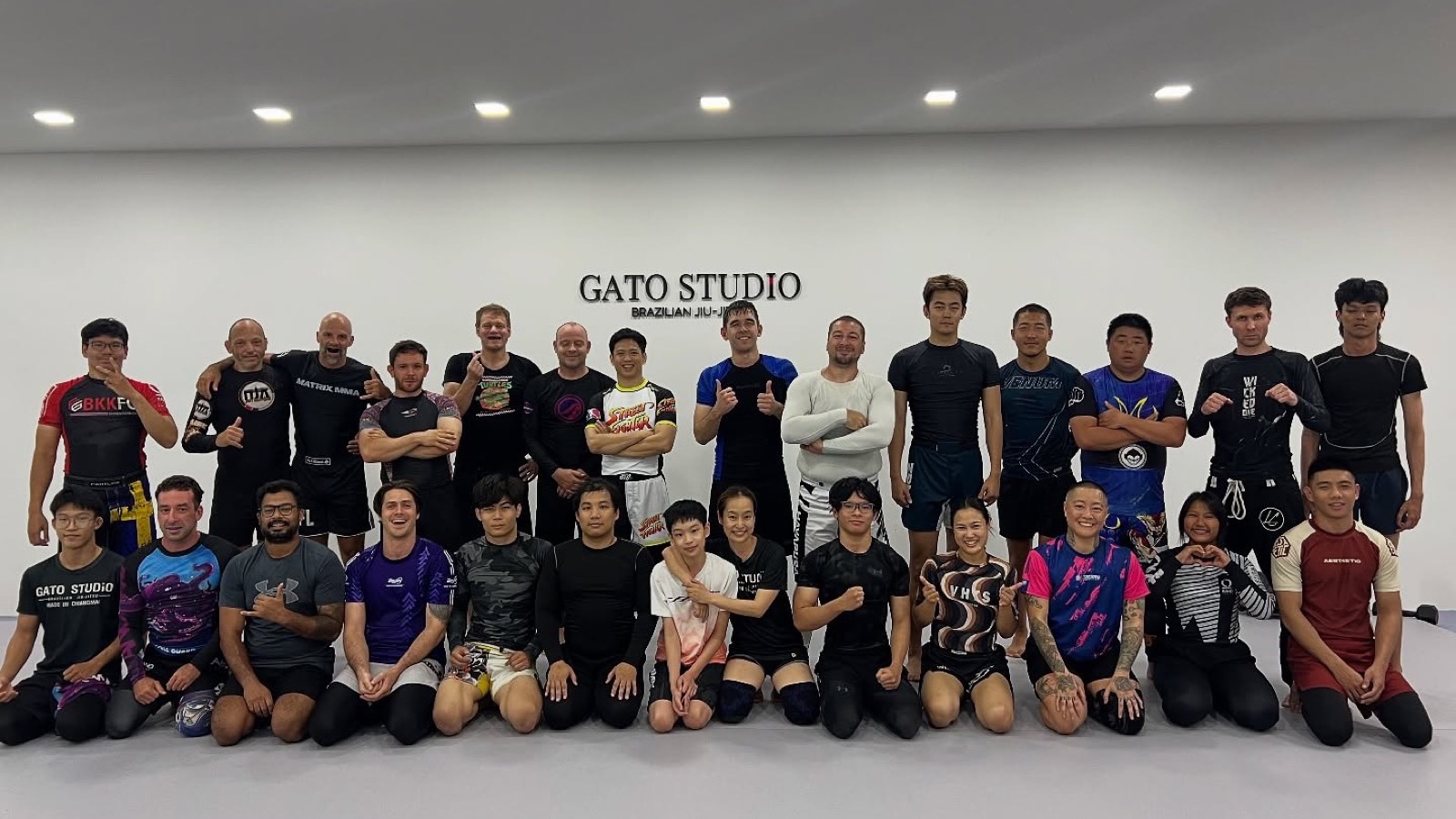 A No-Gi class at Gato Studio BJJ gathered in front of the wordmark wall in Chiang Mai