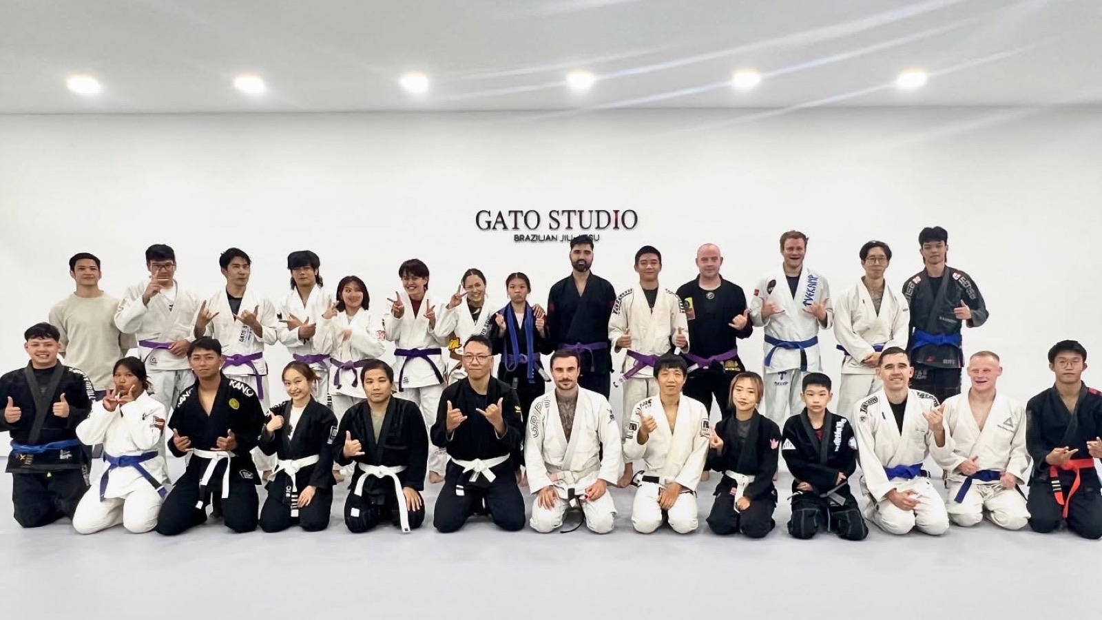 The full class at Gato Studio BJJ lined up together in front of the wordmark wall in Chiang Mai